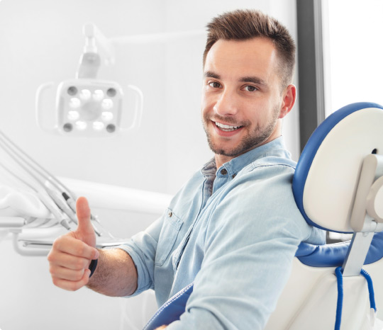 Hip male millennial dental patient gives thumbs up gesture in the dental chair